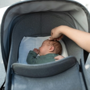 Baby i barnevogn og en hånd som stryker på babyens hode