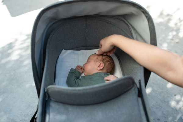 Baby i barnevogn og en hånd som stryker på babyens hode